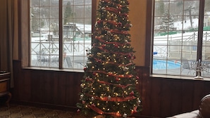 A Christmas tree decorated with lights and ornaments in a room with large windows, a chandelier, and a leather sofa. - Ski-In/Ski-Out at Jiminy Peak  in the Country Inn (Hancock)
