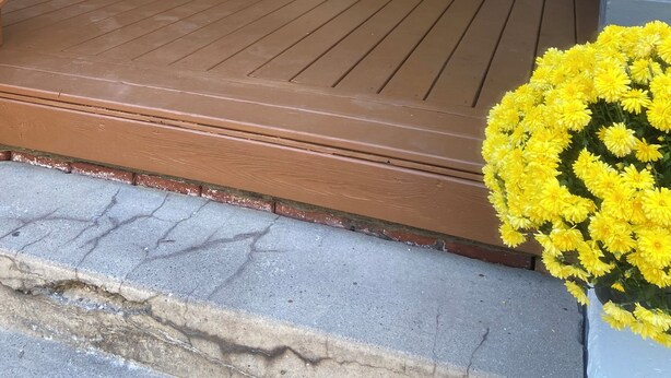 A house with a yellow door, a porch with wooden flooring, and a potted plant.