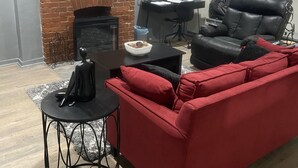 A living room with a red sofa, a black leather chair, a fireplace, a ceiling fan, and a window with blinds.