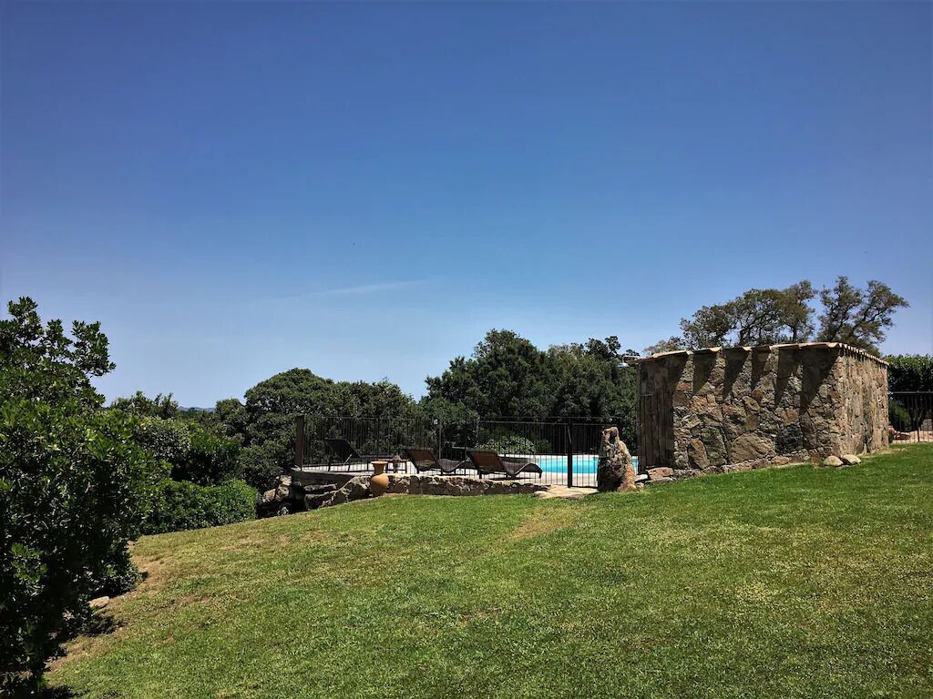 Un'area verdeggiante con una struttura in pietra, una piscina e alberi sullo sfondo.