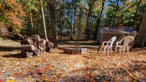 A covered picnic area with a wooden deck, surrounded by trees with autumn foliage. - Small quaint cabin with outside hot tub! sleeps 6! (Kalkaska)