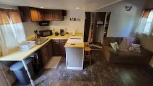 A compact kitchen with a central island, a dining area with a sofa, and a small seating space. - Small quaint cabin with outside hot tub! sleeps 6! (Kalkaska)