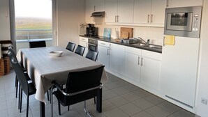 A modern kitchen with white cabinets, a stainless steel microwave, and a dining area with a table and chairs. - PANORAMIC sea, dunes and golf view apartment (Wimereux)