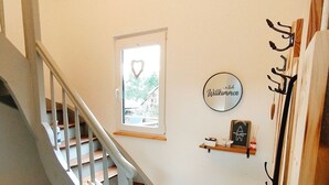 Un escalier avec une rampe blanche mène à un palier. Une décoration en forme de cœur est suspendue à une fenêtre située au-dessus du palier.