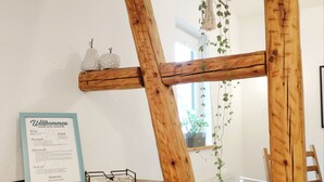 Une pièce aux murs en bois, avec un mur peint en blanc, une pancarte d’accueil encadrée, une petite étagère ornée d’objets décoratifs et une plante suspendue.