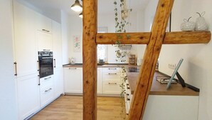 Een keuken met houten balken, witte kastjes en hangplanten.