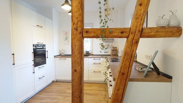 Une cuisine avec des poutres en bois, des meubles blancs et des plantes suspendues.
