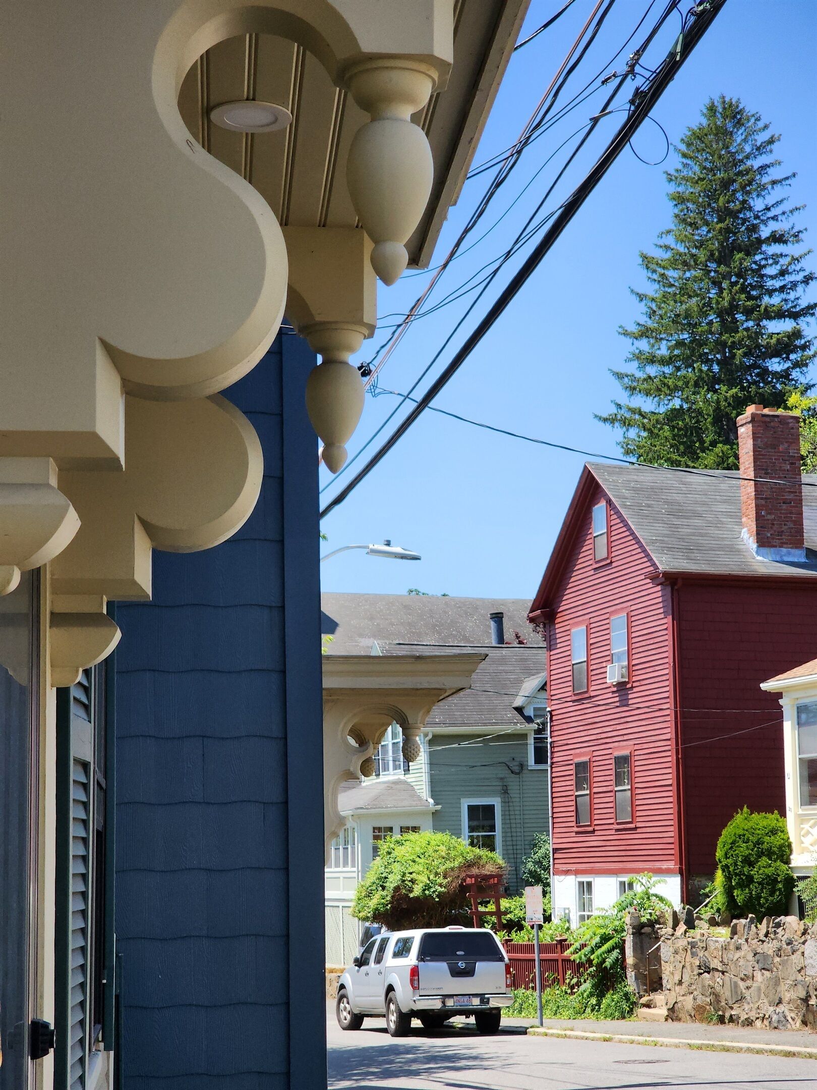 A street view with a white pickup truck parked on the side, a red house, and a blue building with a porch.