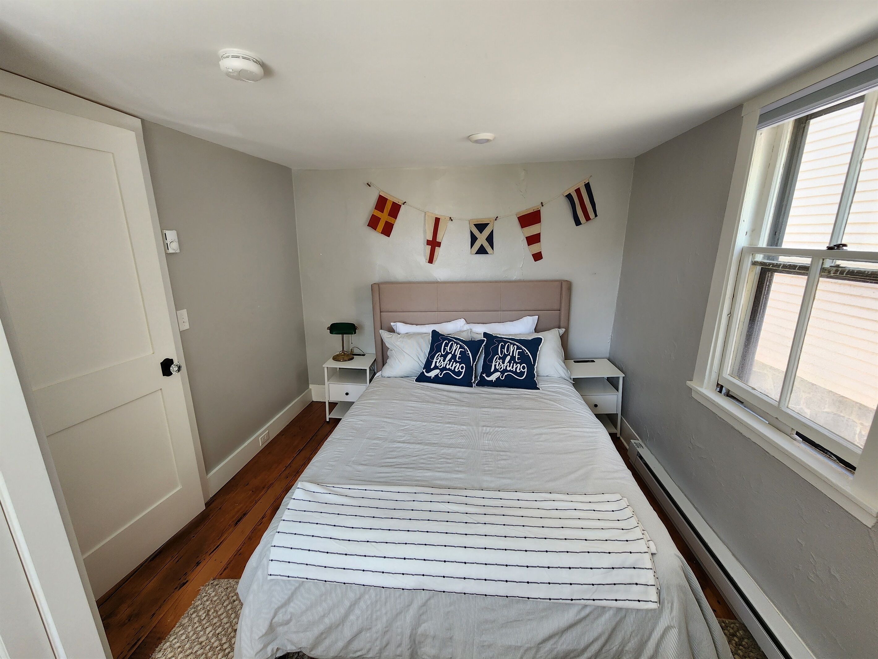 A bedroom with a bed, nightstands, a window, and a wall-mounted flag.