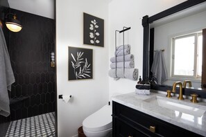 Een moderne badkamer met een douche met zwart-wit betegelde wanden, een wit toilet, een wastafel met gouden kraanwerk en lijstwerken aan de muur.