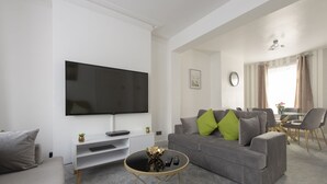 A modern living room with a flat-screen TV, grey sofa, and a coffee table. - Fortified Three Bedroom Home (London)