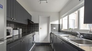 A modern kitchen with dark cabinets, a stainless steel sink, and a window providing natural light. - Fortified Three Bedroom Home (London)