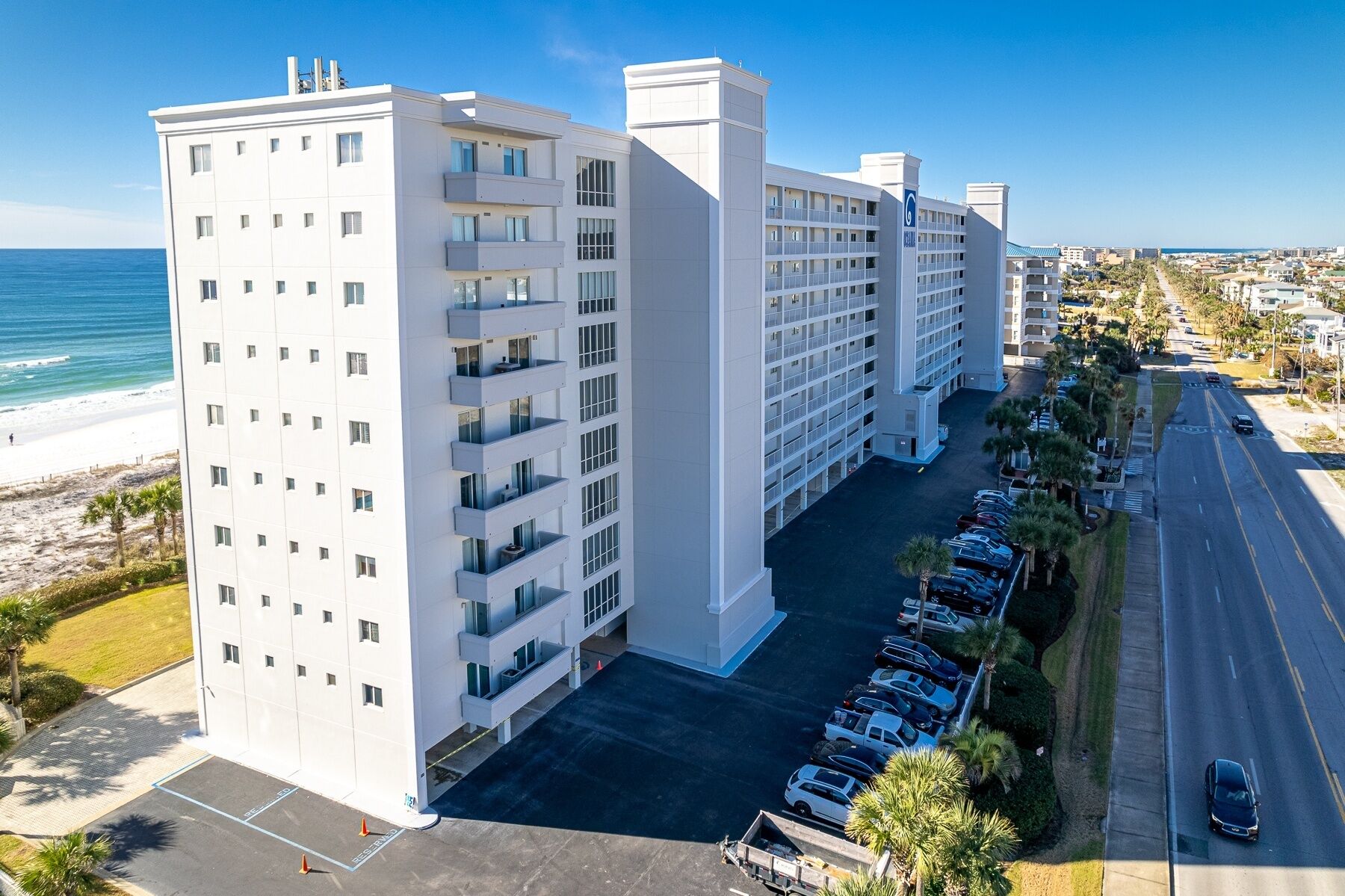 A multi-story hotel with a parking lot and a view of the beach.