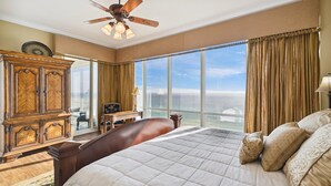 Ein geräumiges Schlafzimmer mit einem großen Bett, einem Holzschrank, einem Schreibtisch und Meerblick durch große Fenster.