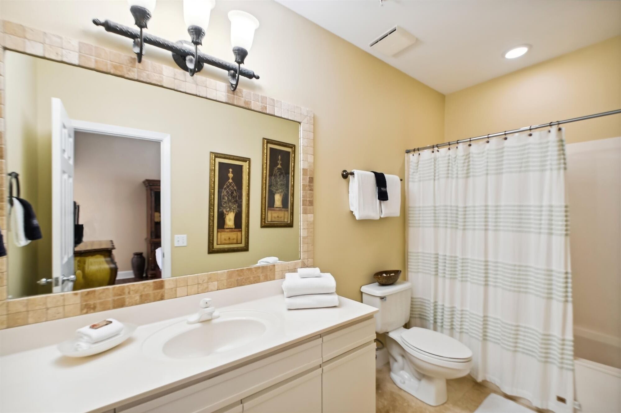 Une salle de bain avec un grand miroir, deux lavabos, des toilettes et un rideau de douche.