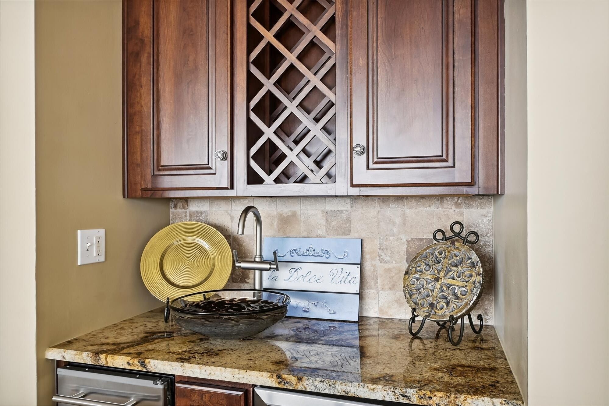 A kitchen with wooden cabinets, a granite countertop, a sink, and decorative items including a plate and a sign.