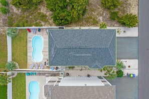 Vista aérea de una propiedad con dos piscinas, un patio cubierto y un edificio grande con techo inclinado.