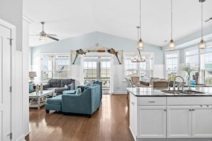 A spacious living area with a large sofa, a dining table, and a kitchen with a central island. - Sea You Soon / 207 Brunswick Ave West 4 Bedroom Home by RedAwning (Supply)