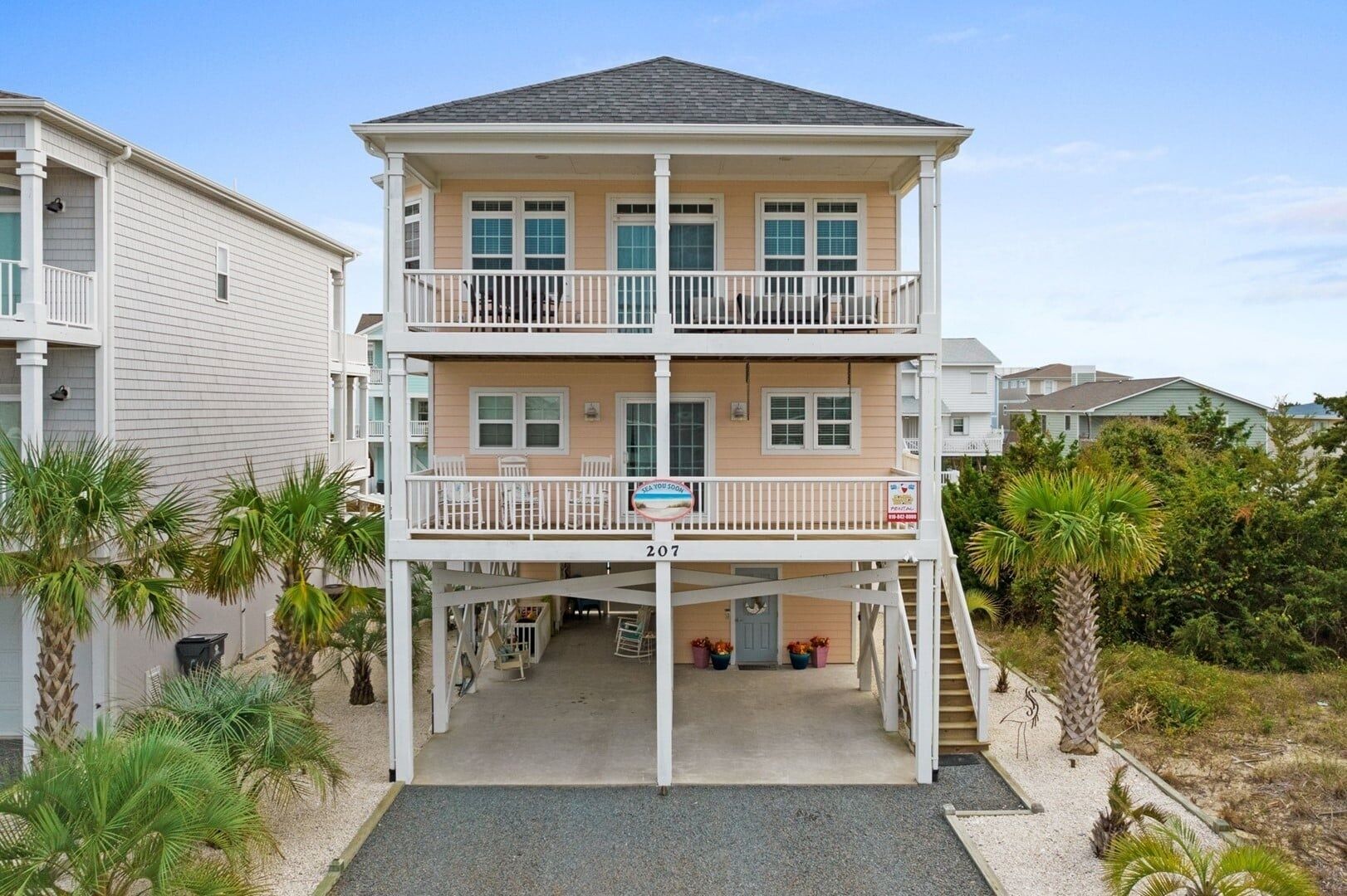 Ein zweistöckiges Strandhaus mit Balkon, einem Schild mit Mietpreisanzeige und der Nummer 207.