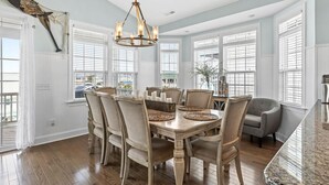 A dining room with a wooden table, chairs, a chandelier, and large windows.