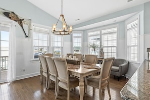 A dining room with a wooden table, chairs, a chandelier, and large windows. - Sea You Soon / 207 Brunswick Ave West 4 Bedroom Home by RedAwning (Supply)
