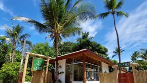 Ingresso di un resort tropicale con cancello in legno, palme e un cartello con su scritto 'LAUS'.