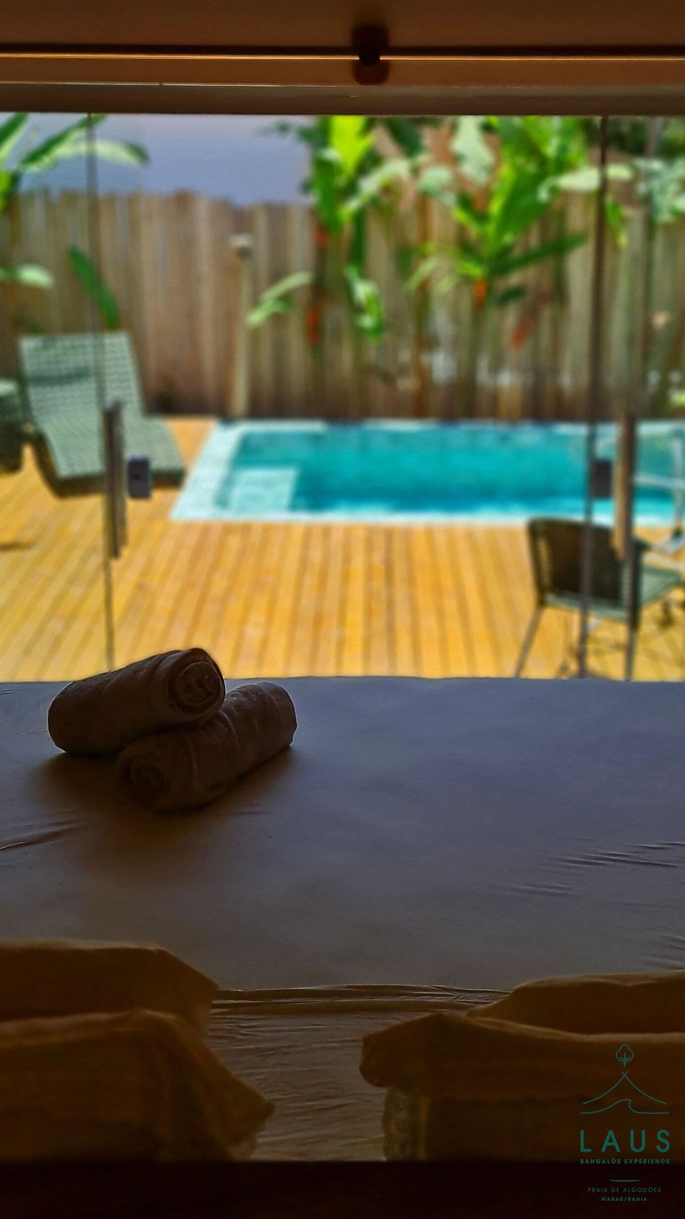 A view of a swimming pool with a wooden deck, a chair, and a towel on a table.