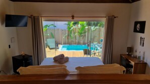 Camera da letto con un letto, una TV, una scrivania e vista su una piscina e mobili da esterno.