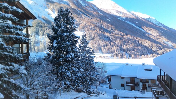 Schneebedeckte Berglandschaft mit einem Holzbau im Vordergrund.