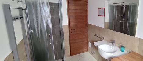 A bathroom with a glass shower enclosure, a wooden door, a sink with a mirror, and a wooden vanity.