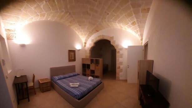 Un dormitorio con techo de piedra, una cama, un escritorio, una silla y un televisor.