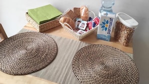 Una mesa de madera con individuales tejidos, una cesta de pan, una botella de agua, un cartón de leche Parmalat y un recipiente con avena.