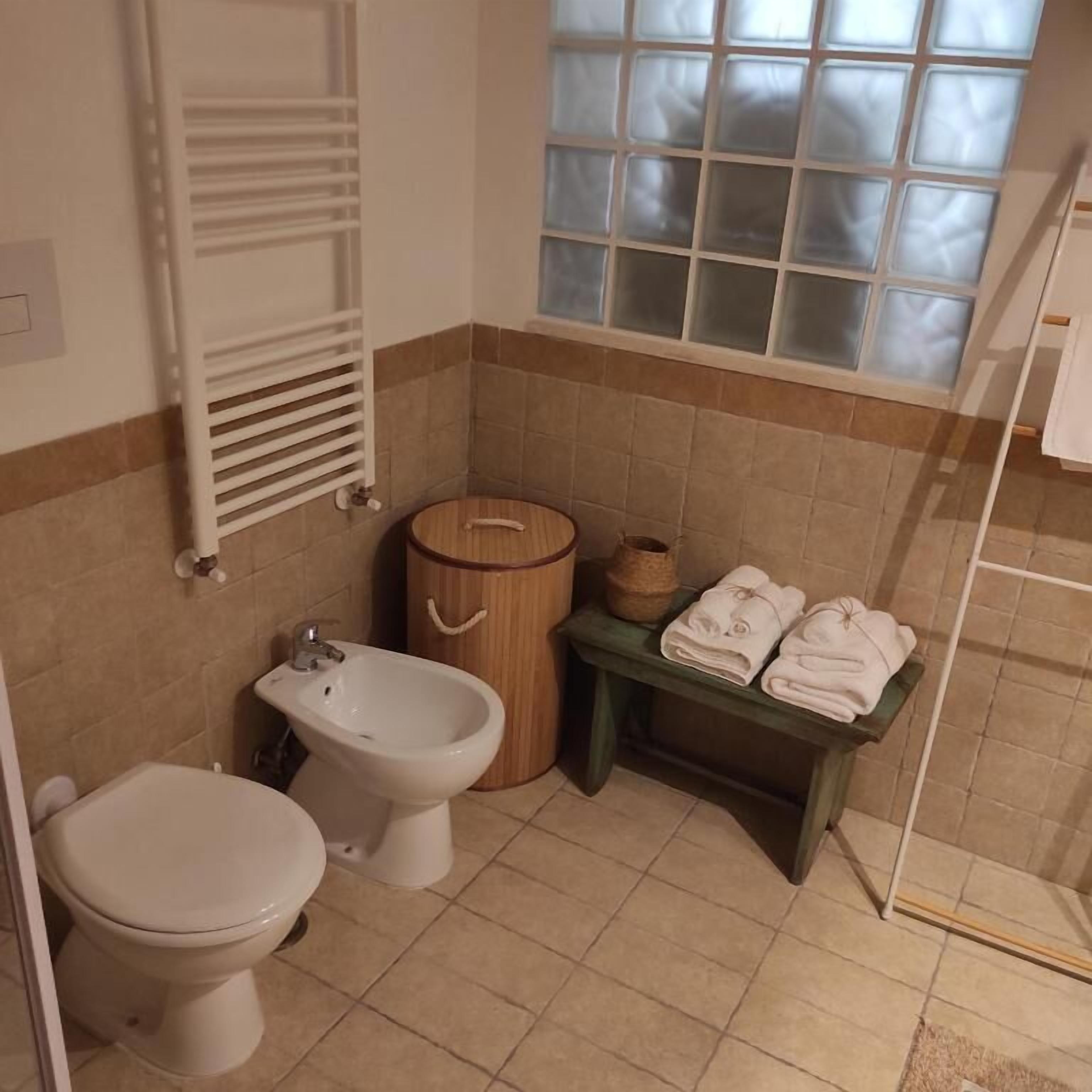 A bathroom with a toilet, bidet, towel rack, and a window with frosted glass.
