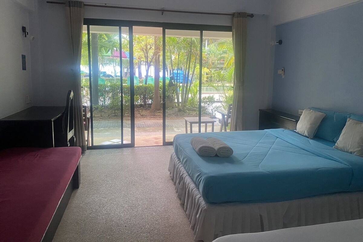 A hotel room with a bed, a desk, and a view of a garden through a sliding door.