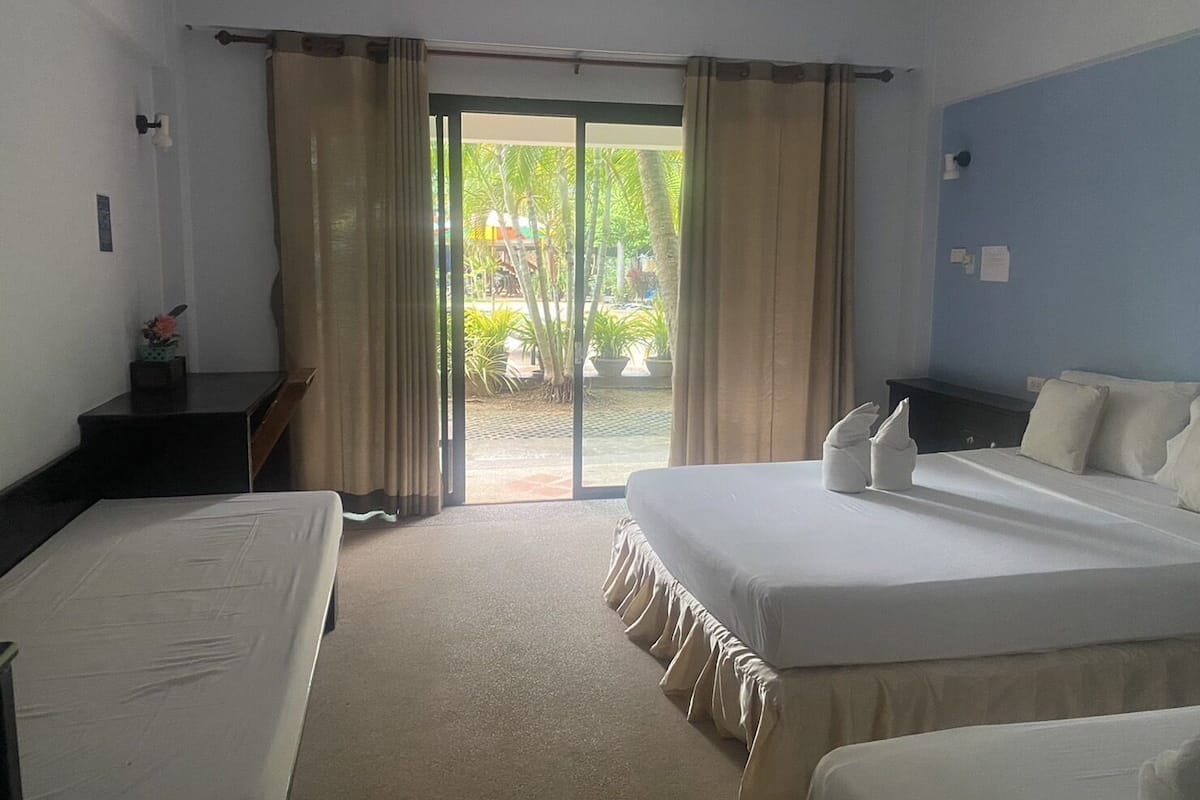 A hotel room with two beds, a desk, and a view of a garden through a sliding door.