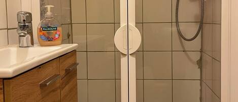 A bathroom with a shower, a toilet, and a sink with a soap dispenser.