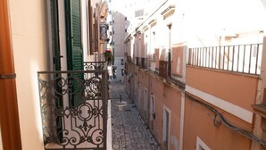 Un estrecho callejón adoquinado entre edificios con balcones, una pequeña mesa con una flor y una barandilla de metal.