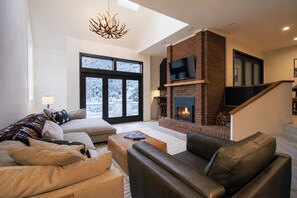 Una sala de estar moderna con chimenea, sofás de cuero, una mesa de centro y un ventanal con vistas a un paisaje nevado.