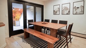 A dining area with a wooden table and chairs, a bench, and a view through a glass door to an outdoor area with autumn foliage. - Fall Family Retreat: Views, Tennis, Fireplace (Stowe)