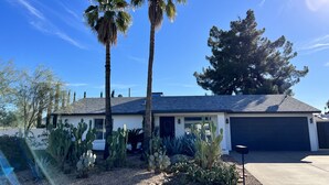 Een woonhuis met garage, omgeven door cactussen en palmbomen.