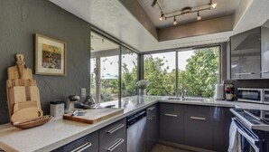 Een moderne keuken met grijze kastjes, een groot raam en een aanrecht met diverse apparaten.