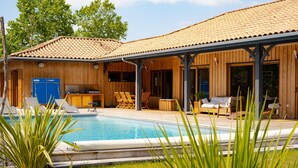Una villa de madera con piscina, mobiliario de exterior y un patio cubierto.