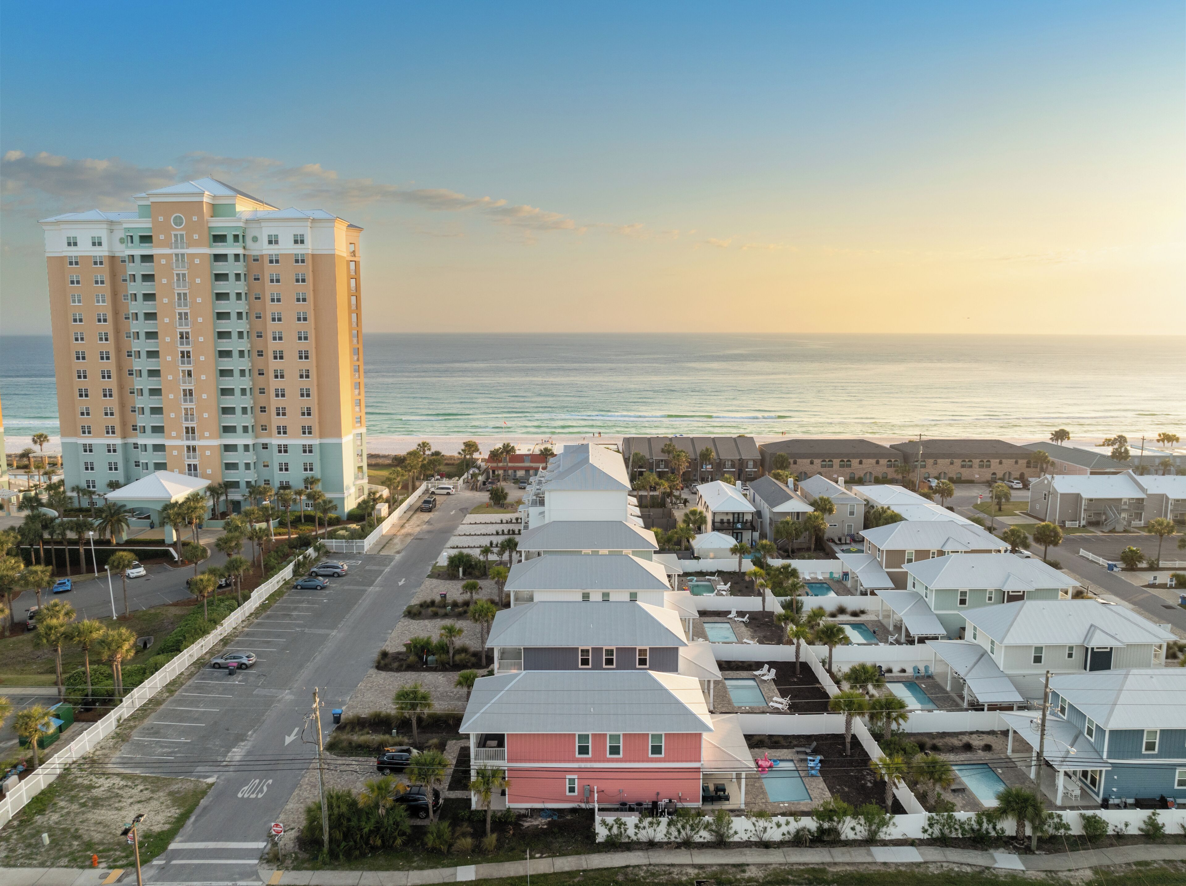 A coastal hotel with multiple buildings, a parking area, and a view of the ocean.