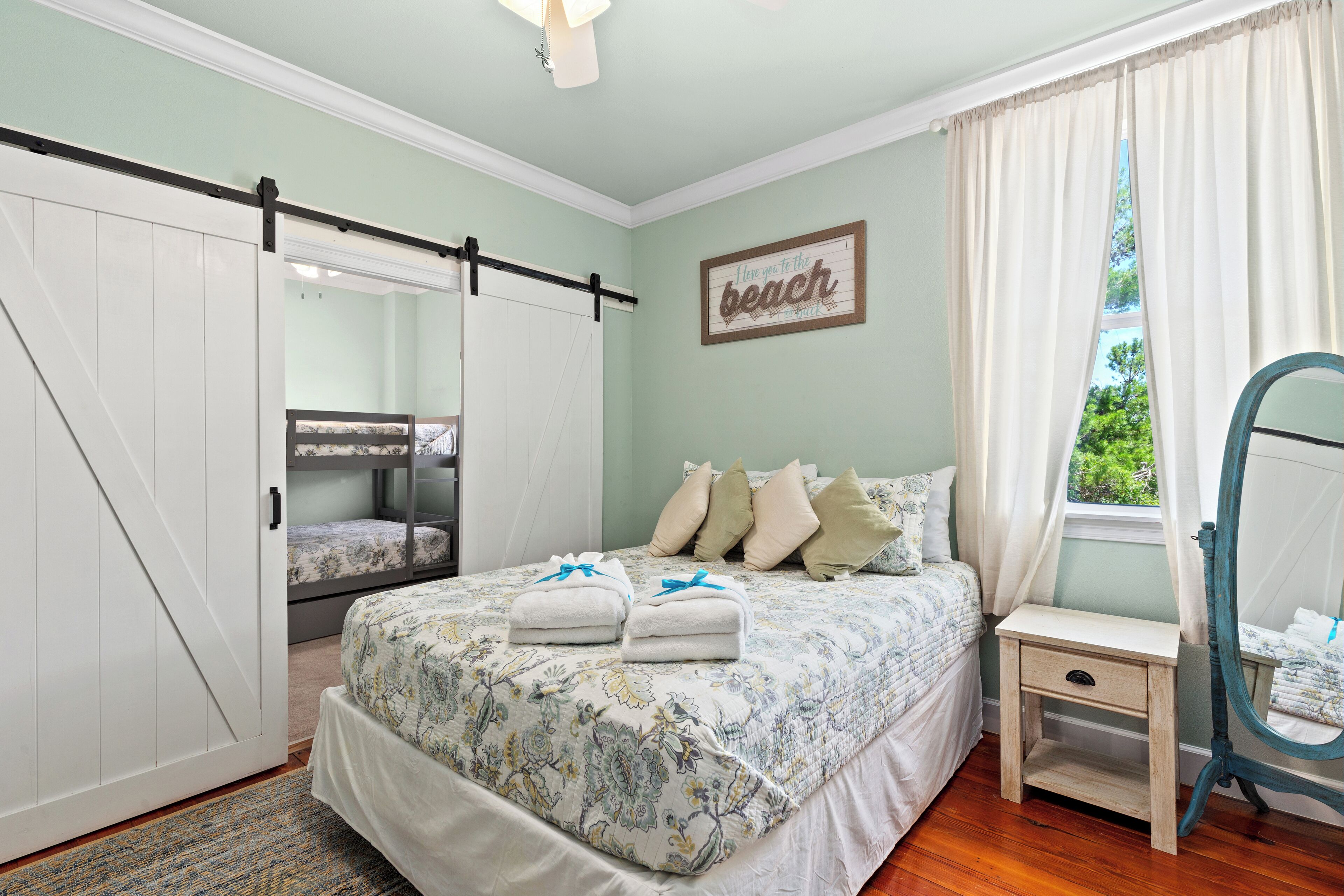 A bedroom with a bed, a bedside table, a mirror, a wardrobe, and a window with curtains.