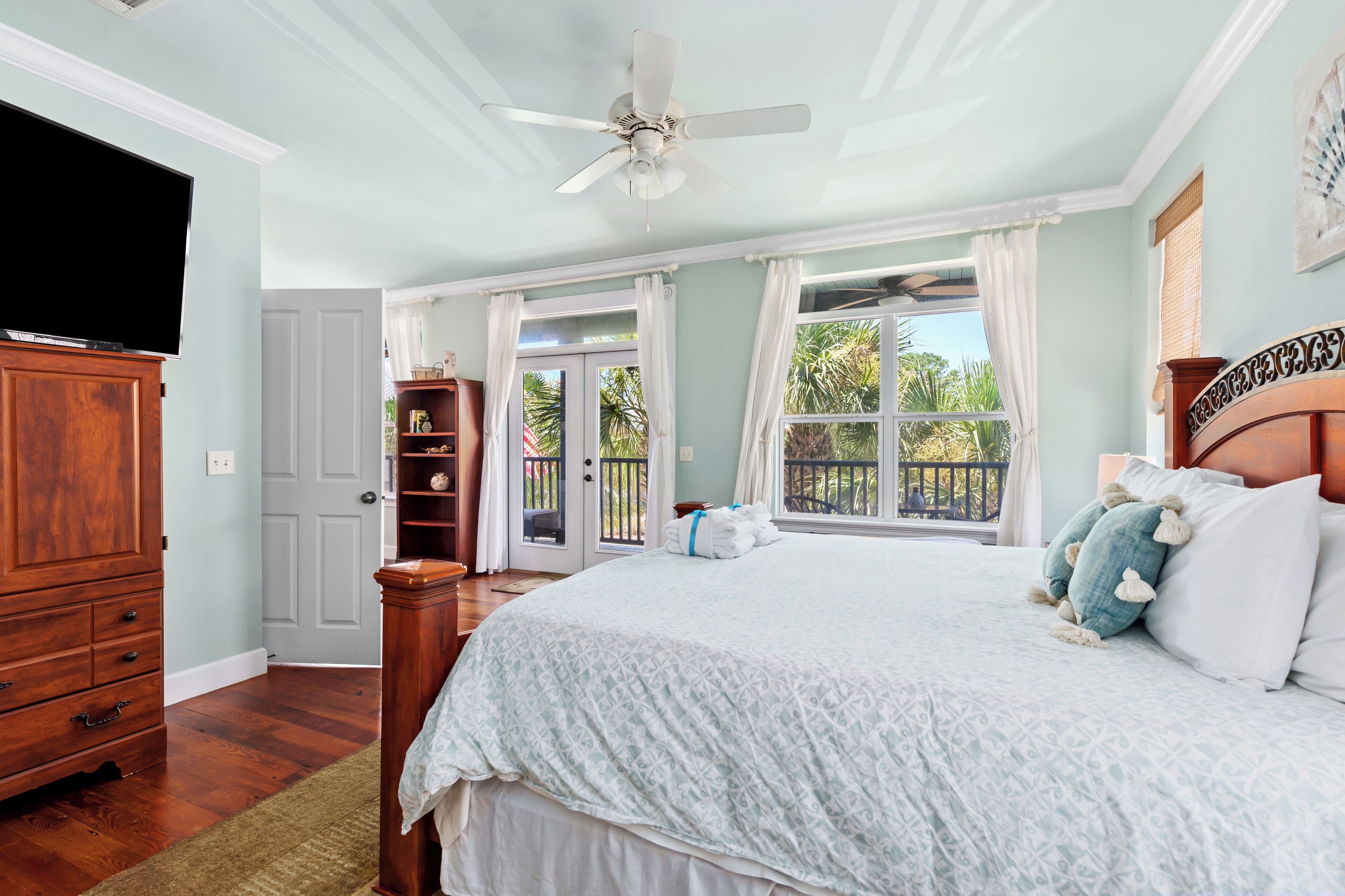 A bedroom with a large bed, a ceiling fan, a wooden dresser, and a TV.