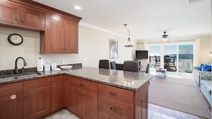 A kitchen with granite countertops, wooden cabinets, a built-in sink, and a dining area with a table and chairs. - Directly On The Beach! First Floor Sundeck! Near Pier Park! Sleeps 6! (Panama City Beach)
