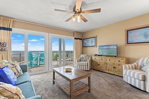 A living room with a ceiling fan, a television, a sofa, a coffee table, and a view of the outdoors. - Breathtaking Views From Gulf Front 2 Bd / 3 Ba Townhome! (Panama City Beach)