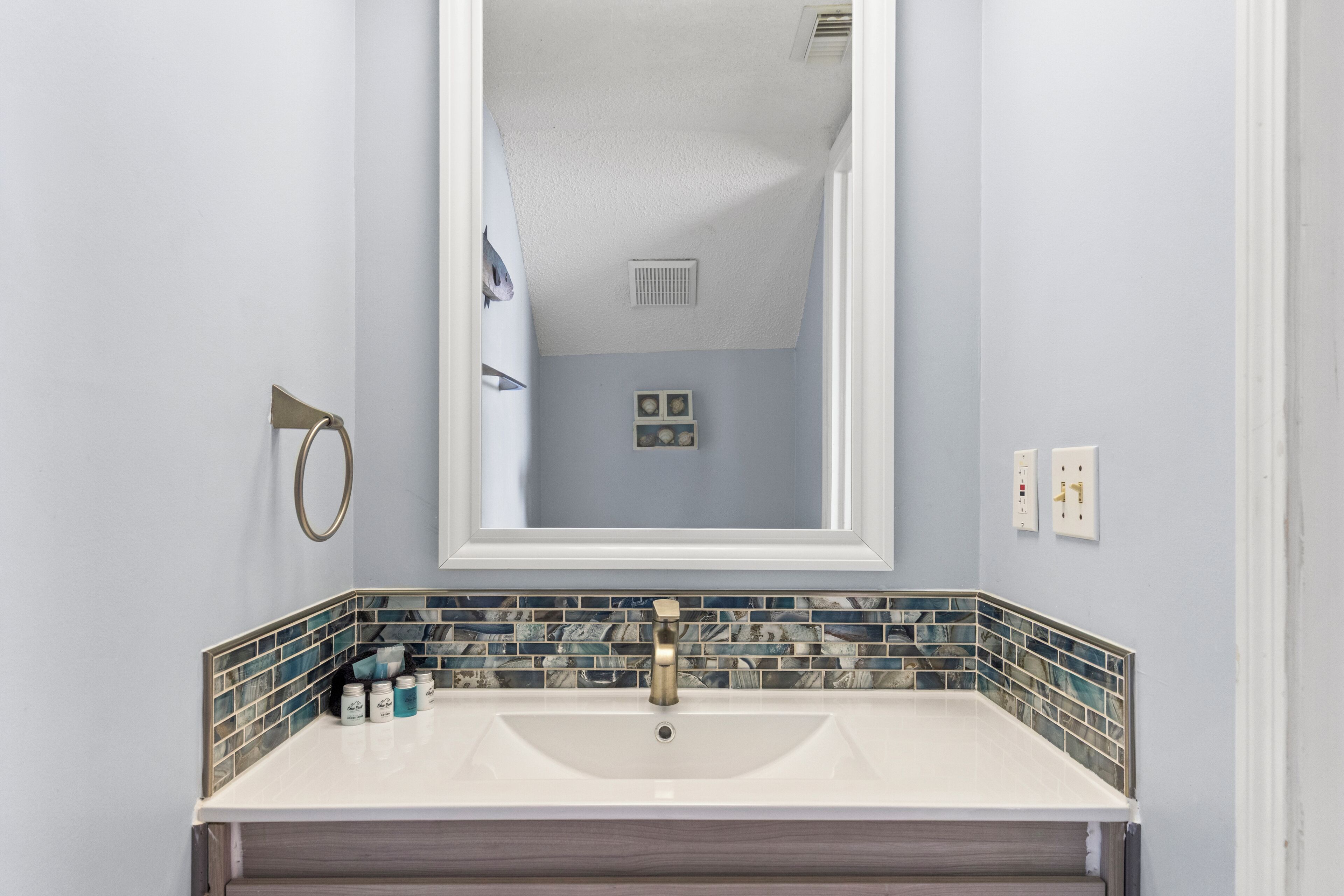 Un baño con lavamanos blanco, un espejo grande y un respaldo de azulejos.