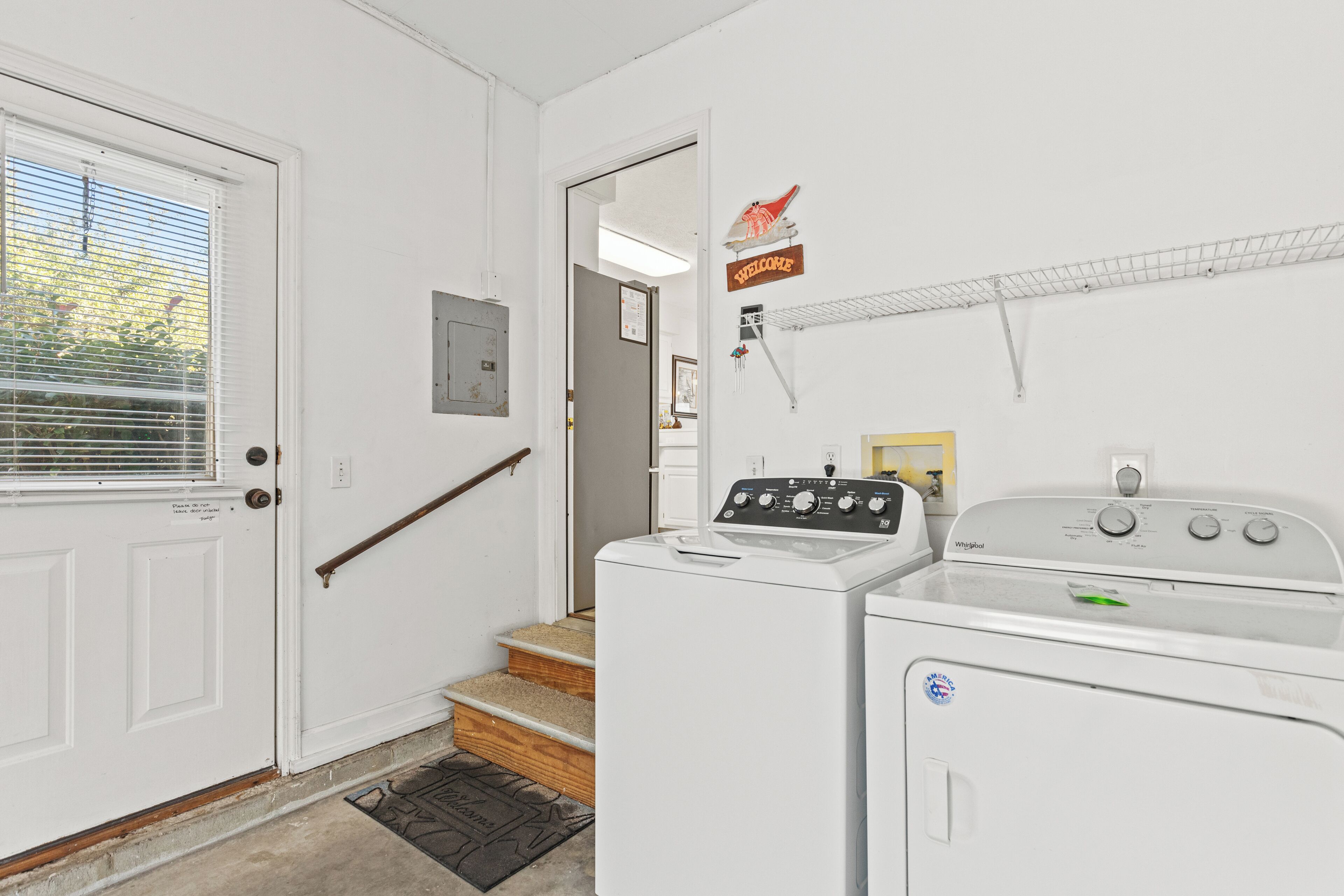 A laundry room with a washer and dryer, a welcome sign, and a staircase leading to another room.