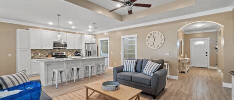 A modern living room with a gray sofa, a wooden coffee table, and a kitchen area with white cabinets and a microwave.